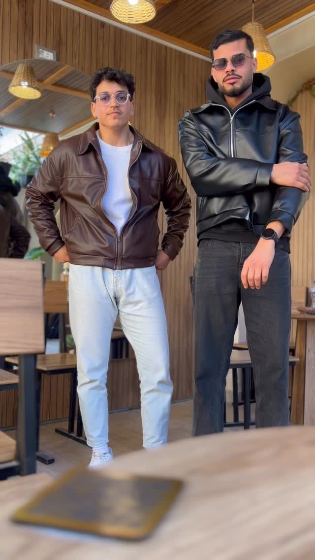 Two men posing while wearing stylish brown and black leather jackets in an indoor setting.