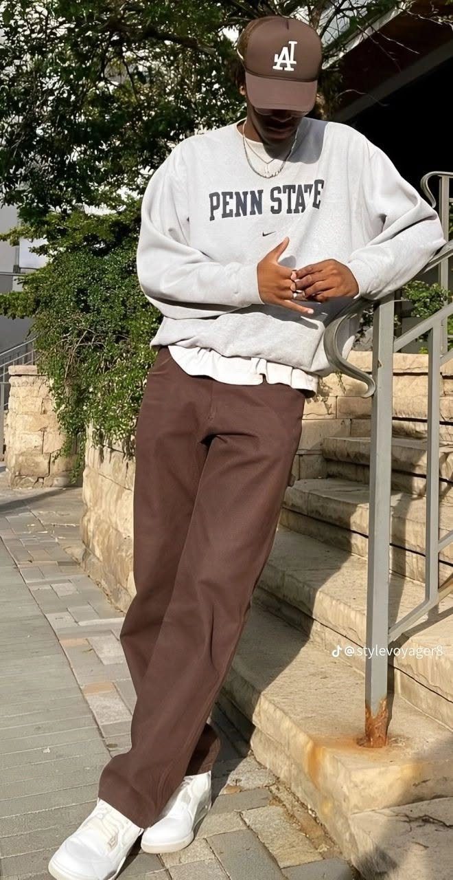 Man in a grey sweatshirt, brown pants, and a baseball cap leaning on stairs.