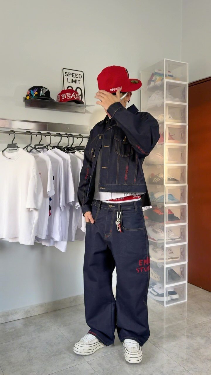 Person posing in a dark denim outfit with a red cap and wide-leg trousers.