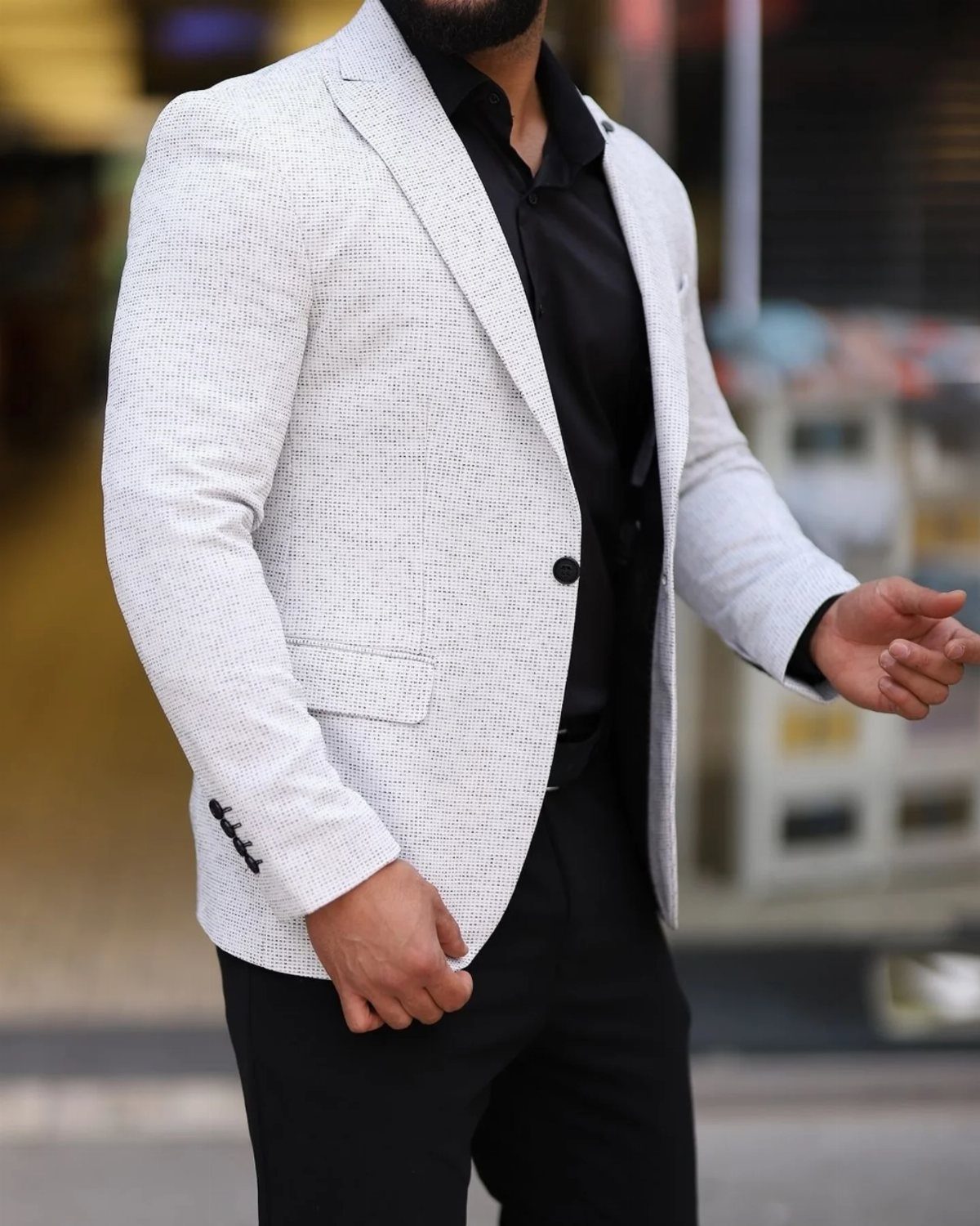 Man wearing a light grey textured blazer over a black shirt and black trousers.