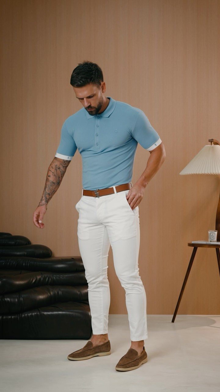 A man wearing a light blue polo shirt and white chinos with brown loafers.