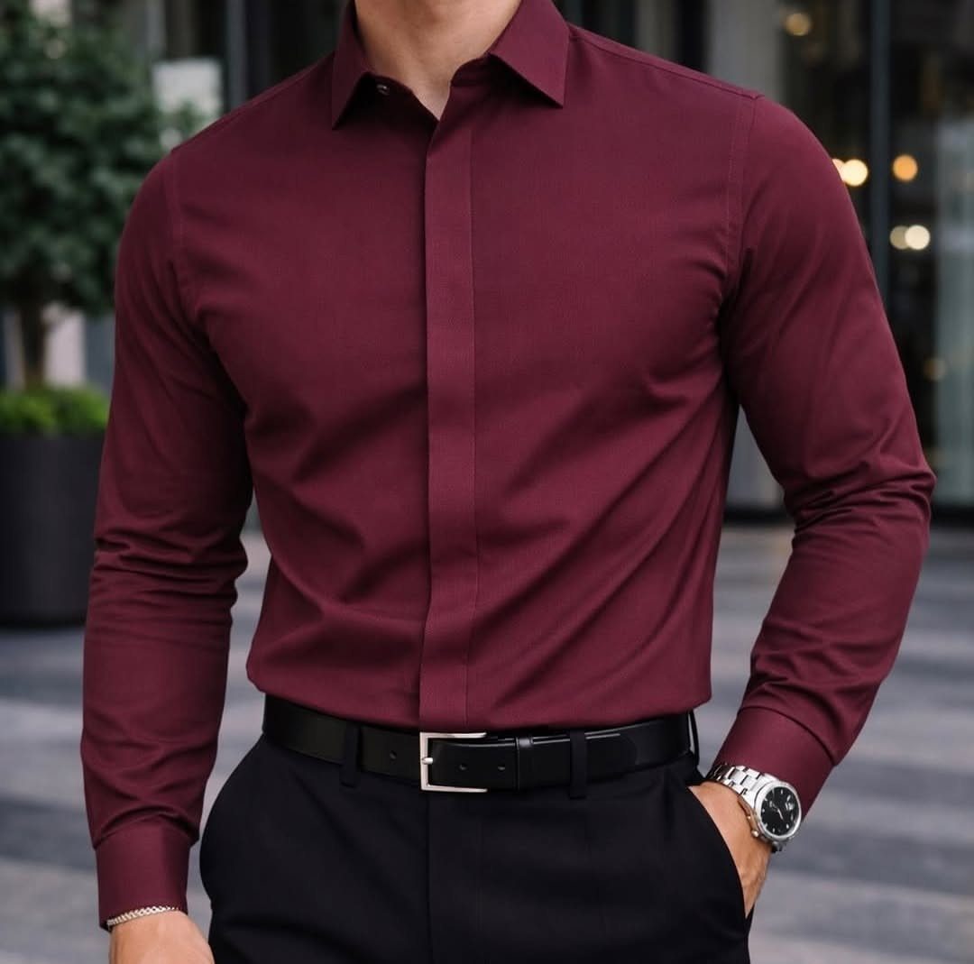 A man wearing a maroon long-sleeved dress shirt tucked into black trousers with a silver watch.
