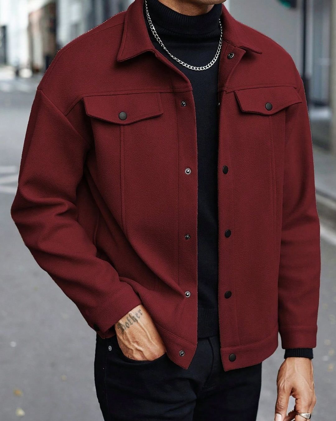 Man wearing a maroon lightweight jacket over a black turtleneck and silver chain necklace.