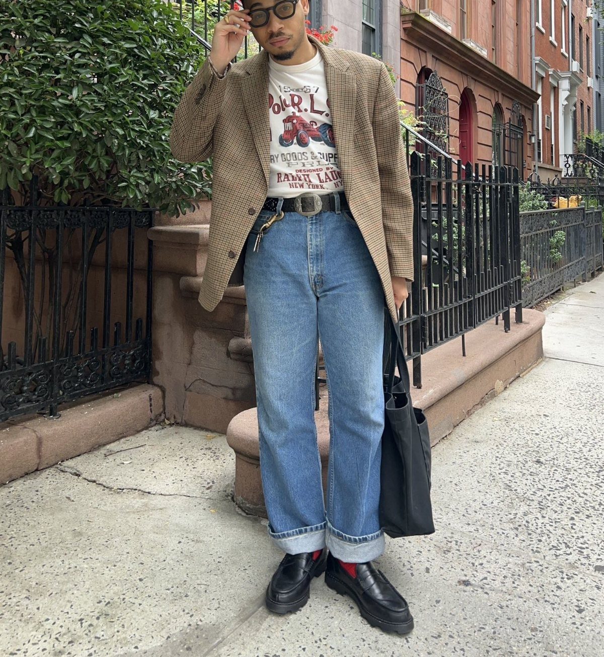 Man wearing a tan blazer, graphic t-shirt, blue jeans, and black loafers on a city street.