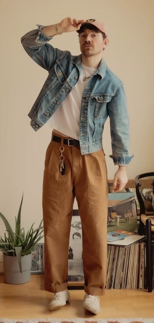Man wearing a denim jacket, white t-shirt, brown trousers, and a pink cap.