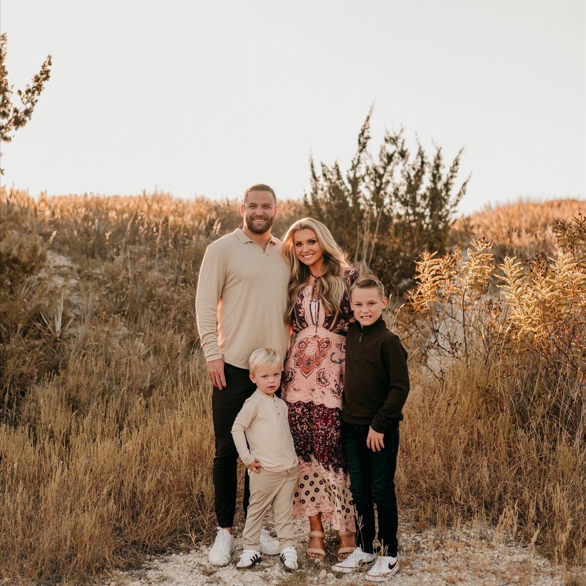 A family of four posing together in a field of tall dry grass at sunset.