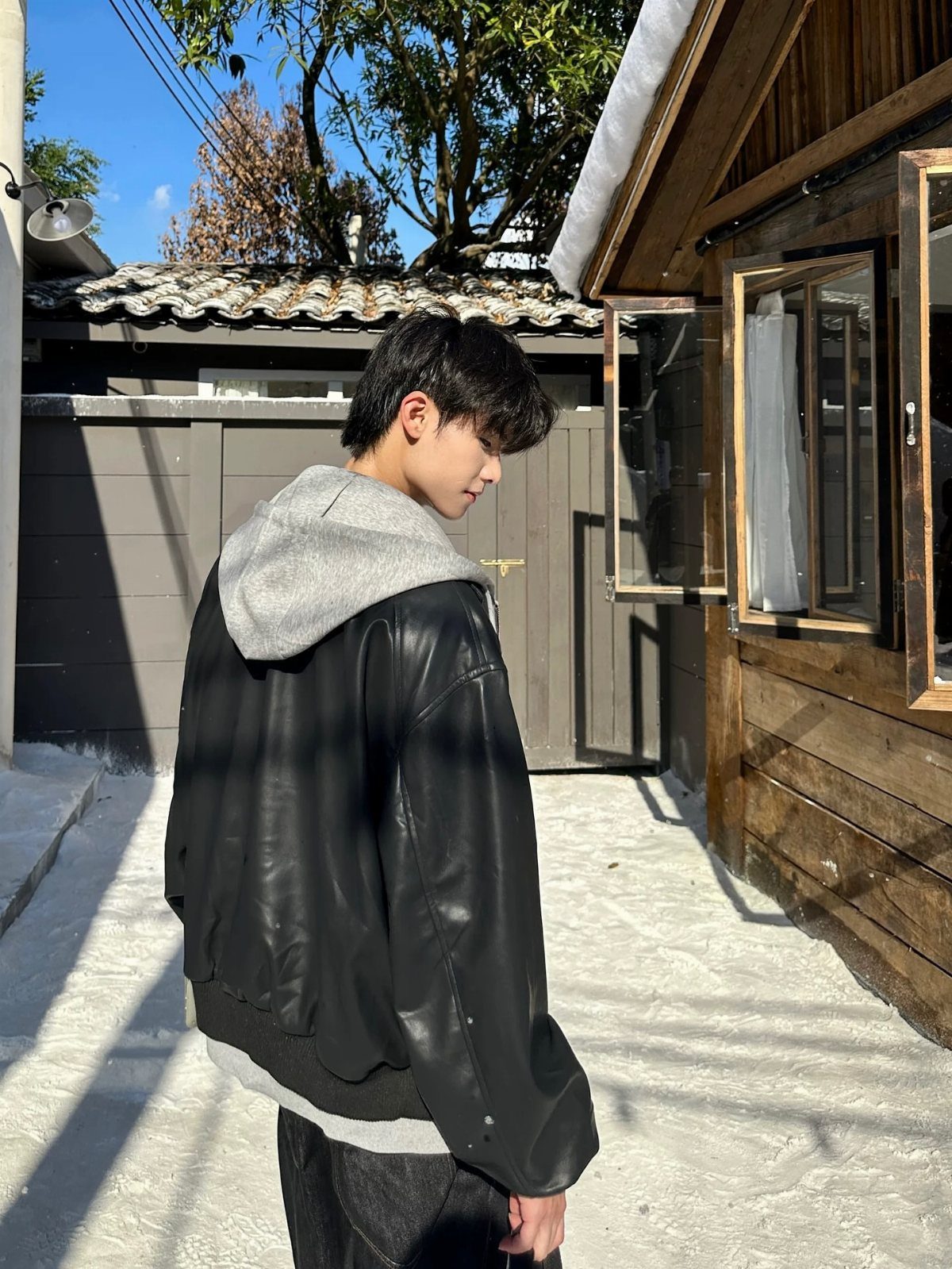 A young man wearing a grey oversized hoodie and a black leather jacket standing outdoors.