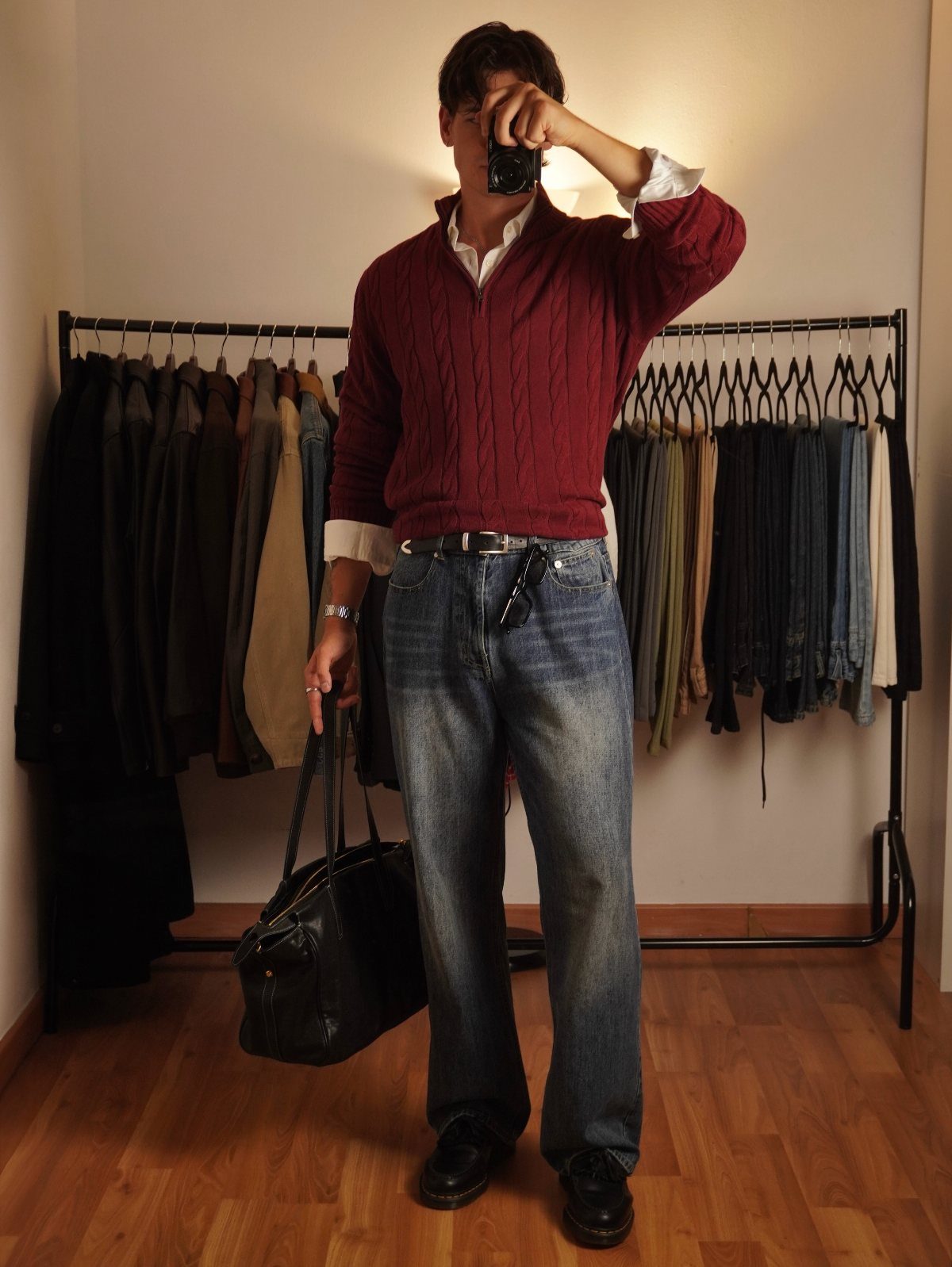 Man wearing a burgundy cable-knit sweater layered over a white collared shirt and blue jeans.