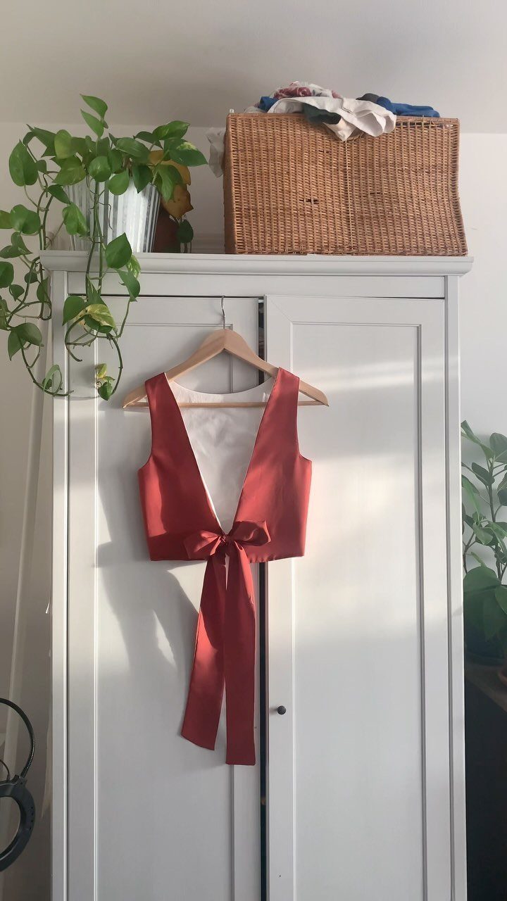A reddish-brown satin sleeveless top with long ties hanging on a wooden hanger.