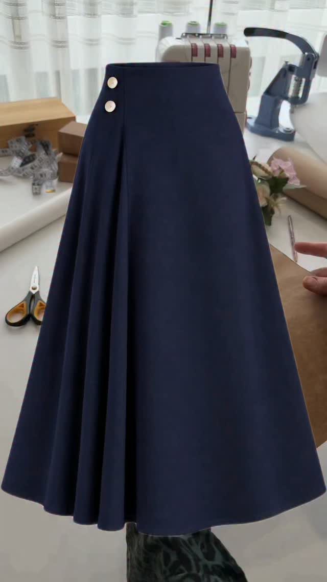 A navy blue pleated skirt with gold buttons displayed on a mannequin in a sewing studio.