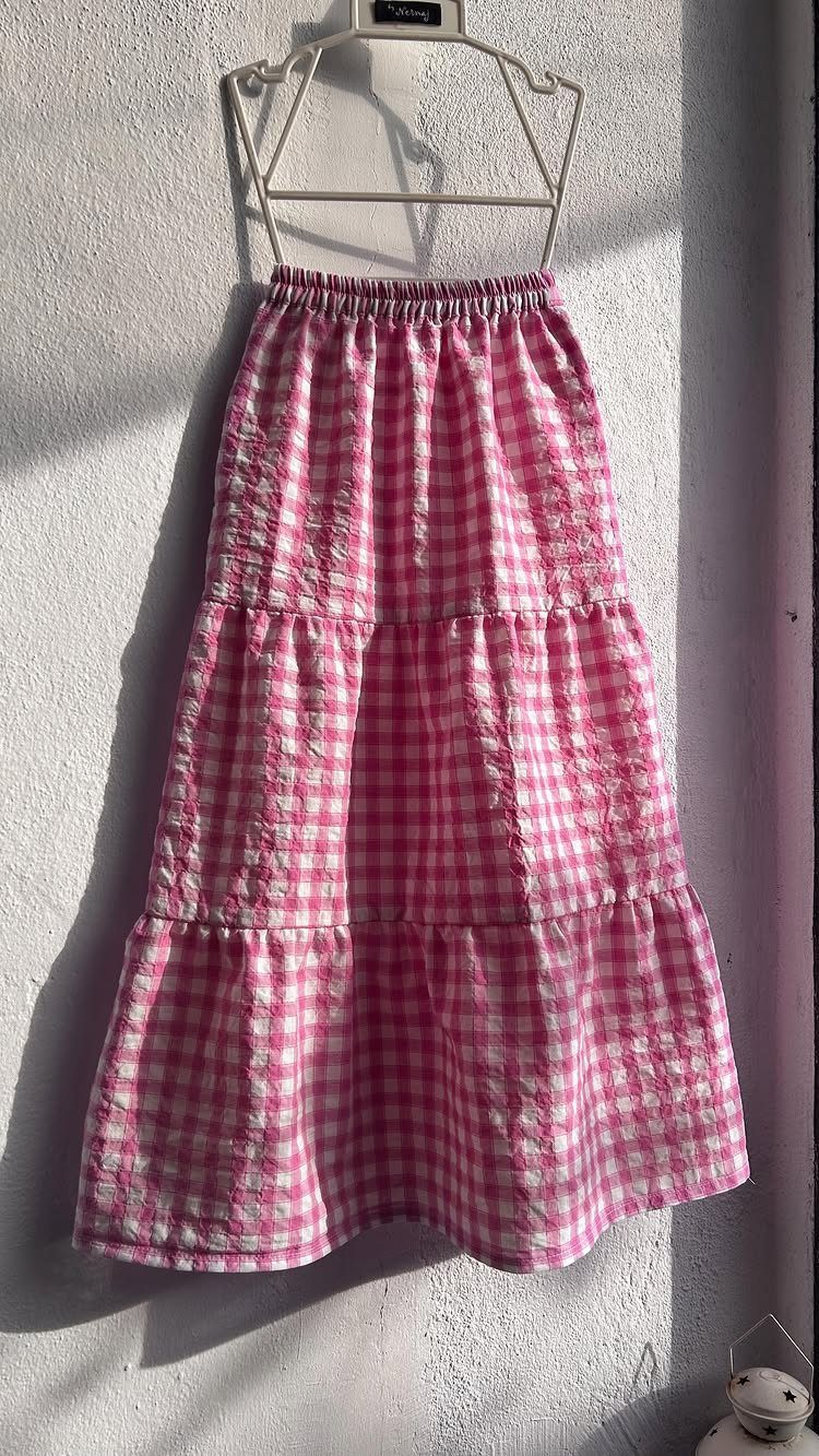 Pink and white gingham checkered tiered maxi skirt hanging on a white wire hanger.