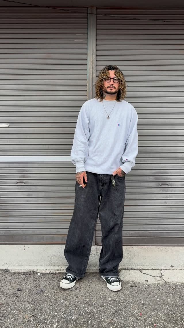A man wearing baggy streetwear and sneakers posing in front of a grey metal garage door.