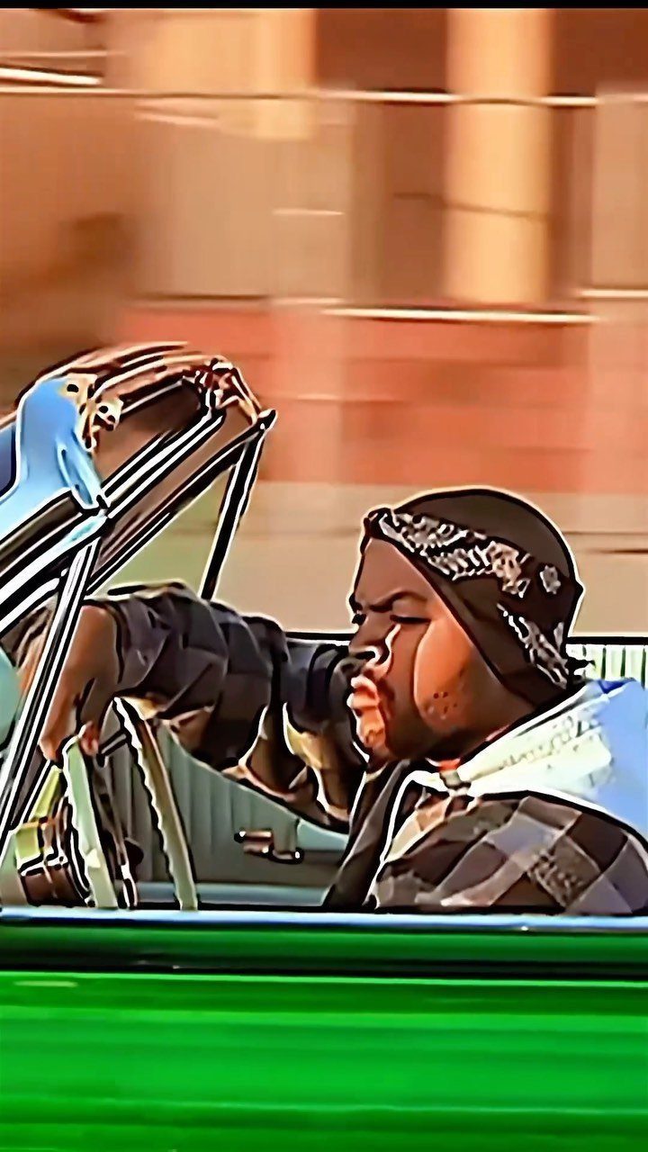 A man in a bandana driving a car through a blurred urban setting.