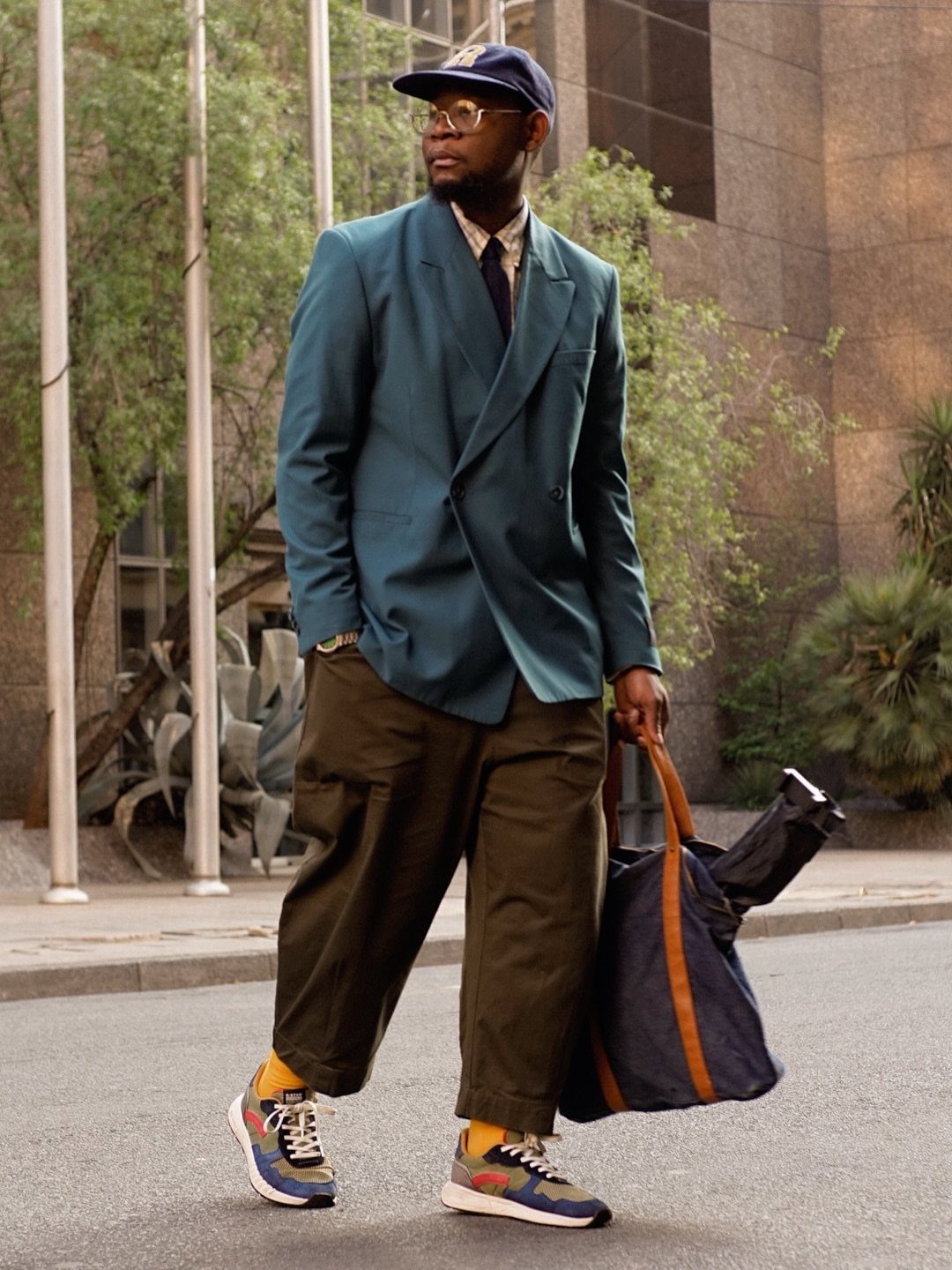 A man walking outdoors wearing a teal blazer, olive green cargo pants, and colorful sneakers.