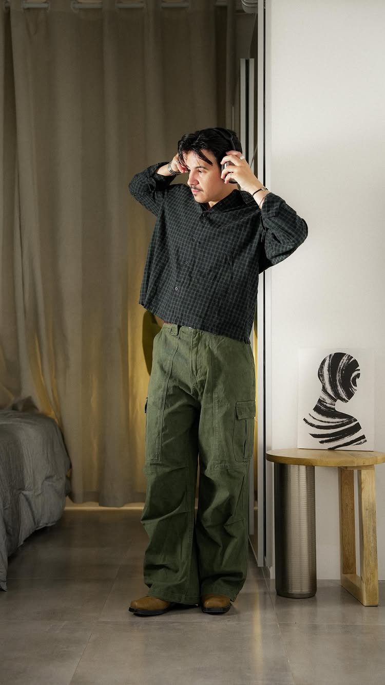 A man posing in a dark patterned shirt and wide-leg green cargo pants.