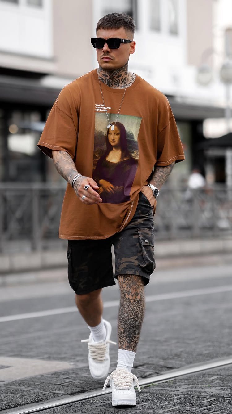 Man walking in a city wearing a brown graphic t-shirt and camouflage cargo shorts.