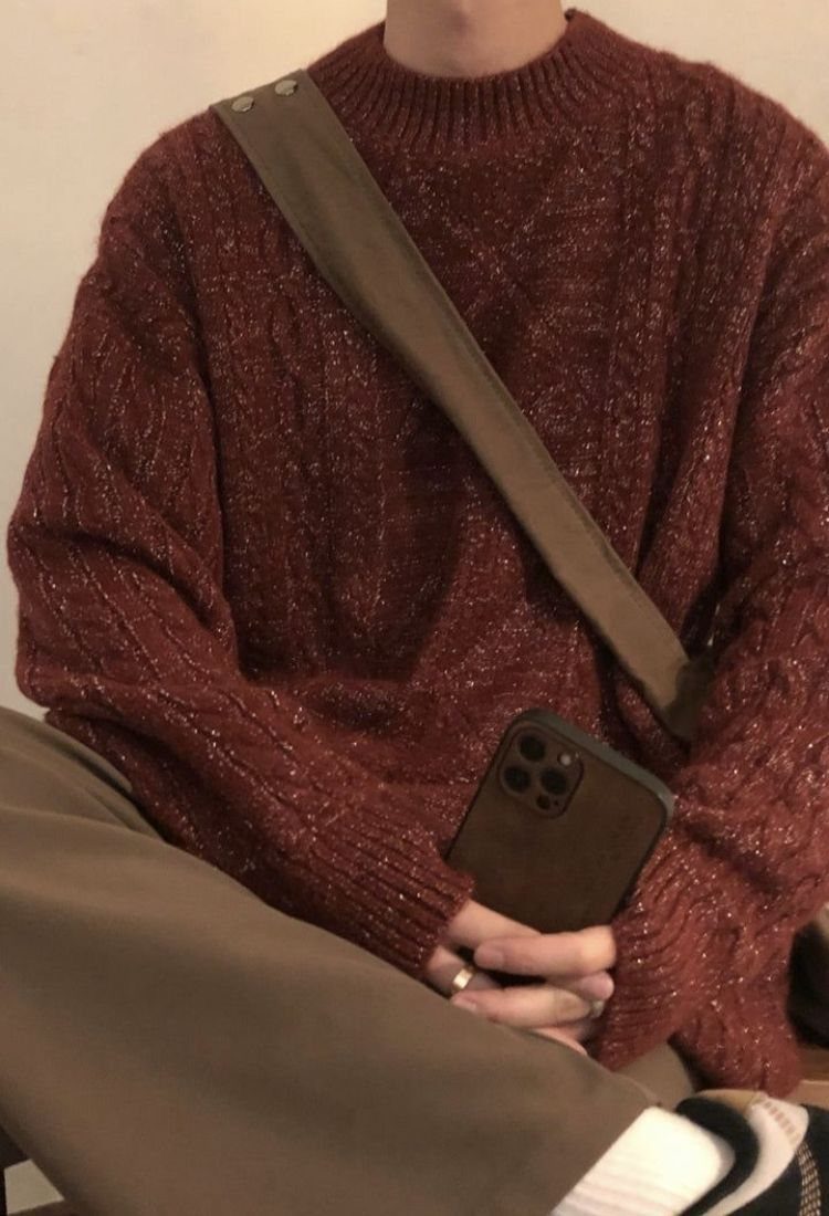 A person wearing a reddish-brown cable-knit sweater and tan trousers with a crossbody bag.
