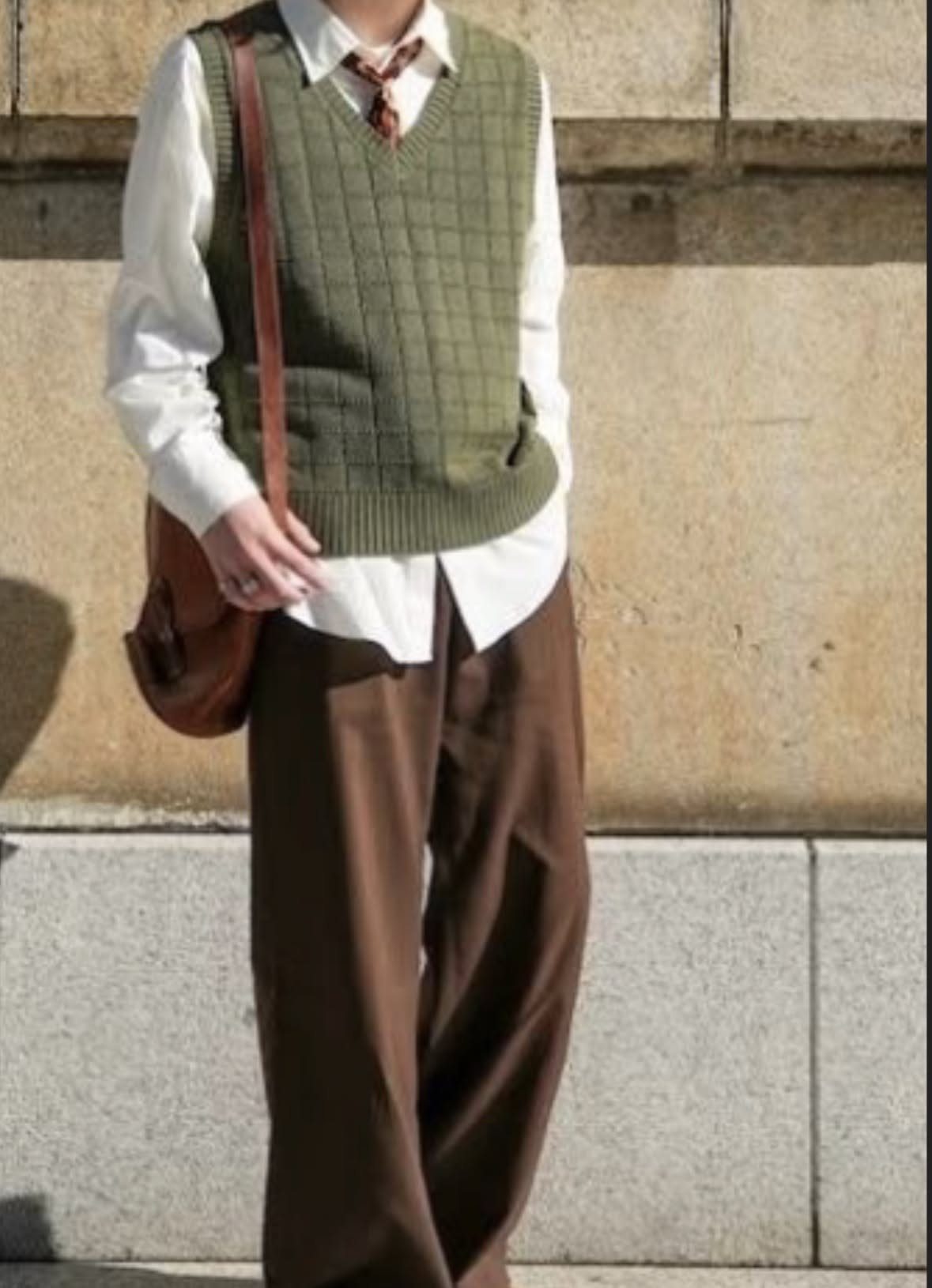 A person wearing a white shirt, green sweater vest, and wide-leg brown trousers.