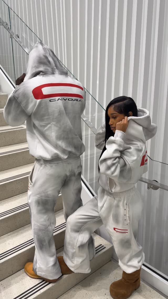 Two people posing on stairs wearing matching white and red tie-dye sweatsuits.