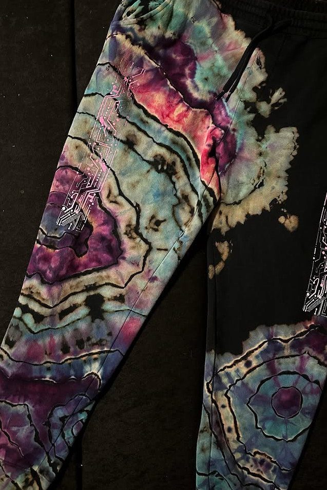 Tie dyed black sweatpants with colorful purple, pink, and teal swirling patterns laid on a dark surface.