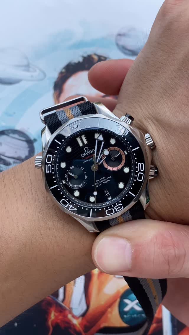 A silver Omega wristwatch with a black dial and a striped NATO strap on a person's wrist.