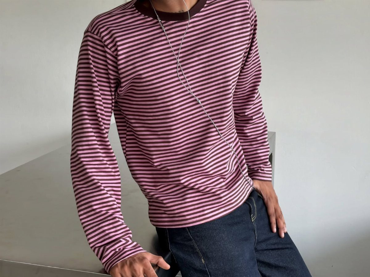 Man wearing a maroon and pink striped long-sleeved tee and dark denim jeans.