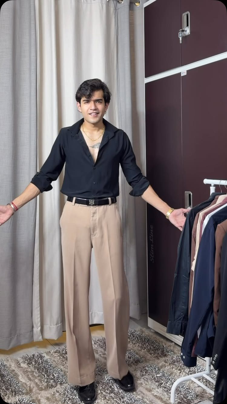 A young man posing in a black button-down shirt and tan wide-leg trousers.