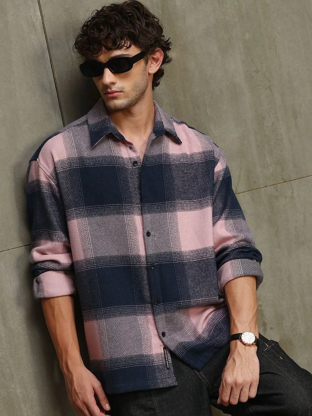 A man wearing a pink and navy blue checked button-down shirt and sunglasses.