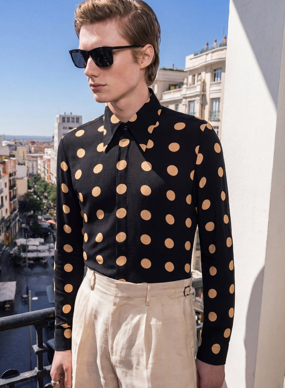 A man wearing a black shirt with large tan polka dots and cream trousers.