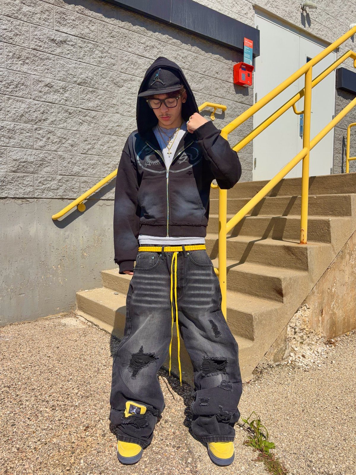 A person wearing baggy distressed black jeans and an oversized black hoodie standing on outdoor stairs.
