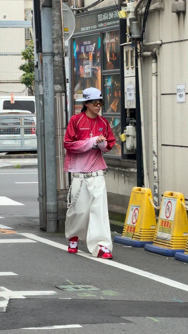 Person walking in a city wearing baggy white pants, a gradient shirt, and a white cap.