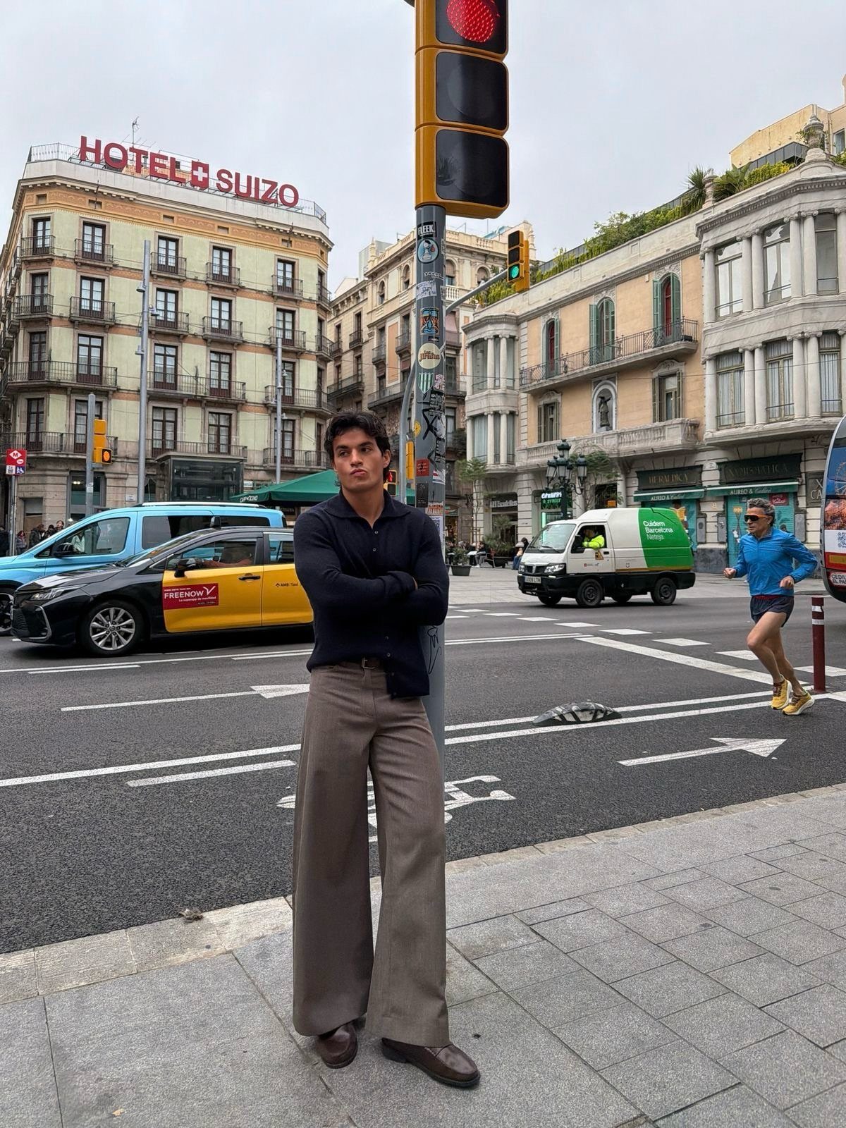Man standing on a city street wearing wide-leg tan vintage trousers and a dark shirt.