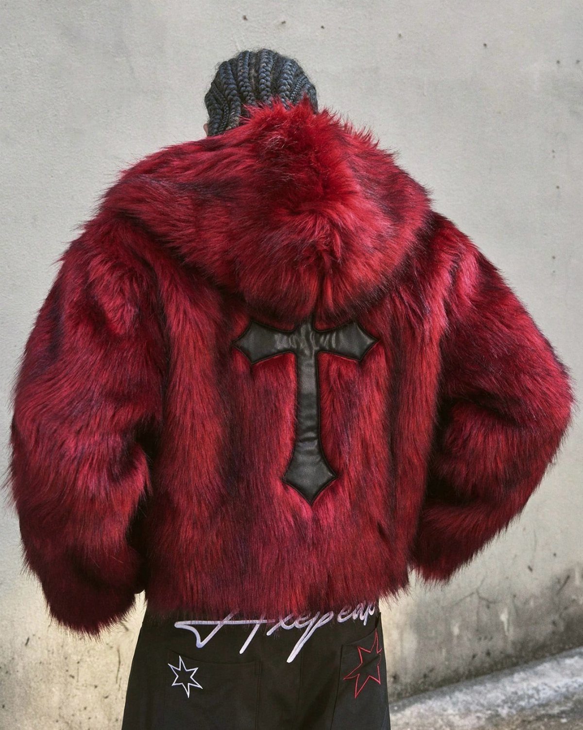 Person wearing a bright red faux fur hooded jacket with a black cross on the back.