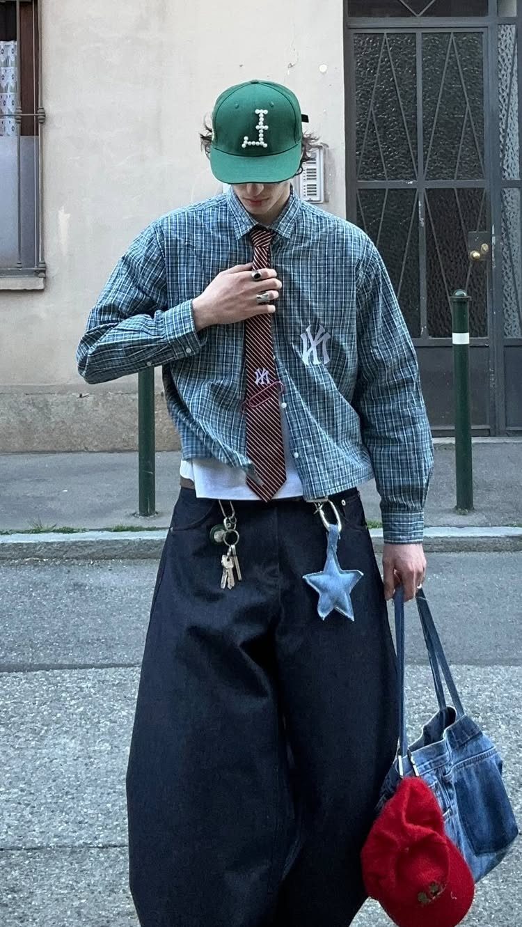A person wearing an oversized checkered shirt, a tie, and extremely baggy black trousers outdoors.