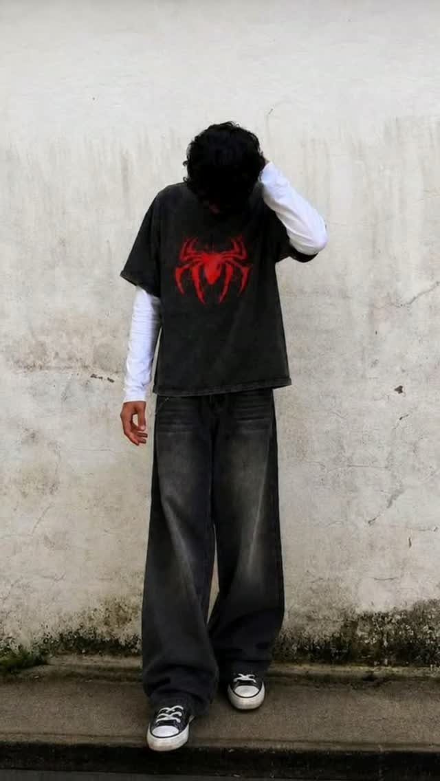 A person wearing a red spider graphic t-shirt, white long sleeves, and baggy grey jeans.