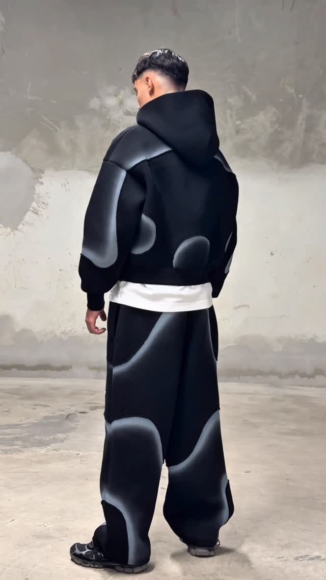 Man wearing oversized black streetwear with large grey organic patterns and wide-leg trousers.