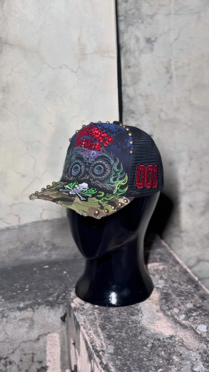 A decorated black baseball cap with red rhinestones and skull graphics on a black mannequin head.