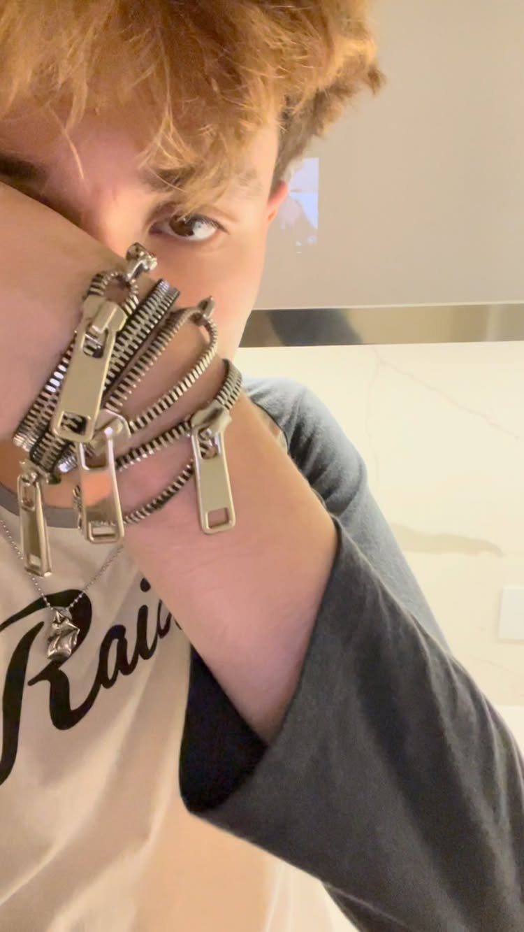 Young man wearing silver zipper bracelets and a graphic t-shirt while posing for a selfie.