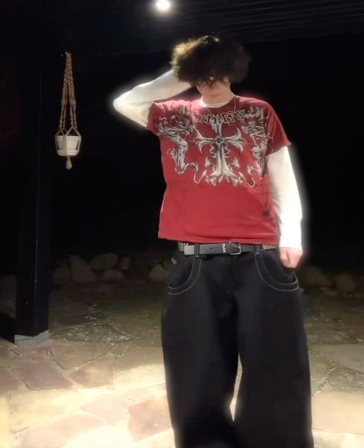 Person wearing a red graphic t-shirt and baggy black pants with white stitching.