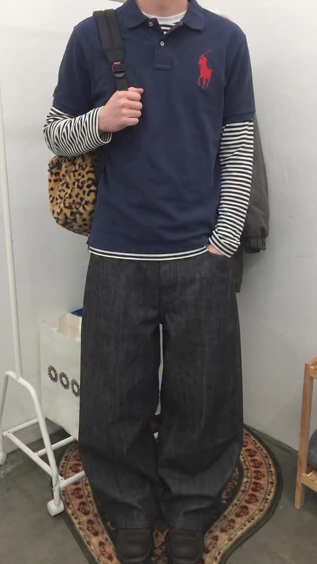 Person wearing a navy polo, striped long-sleeve shirt, and baggy dark denim jeans.