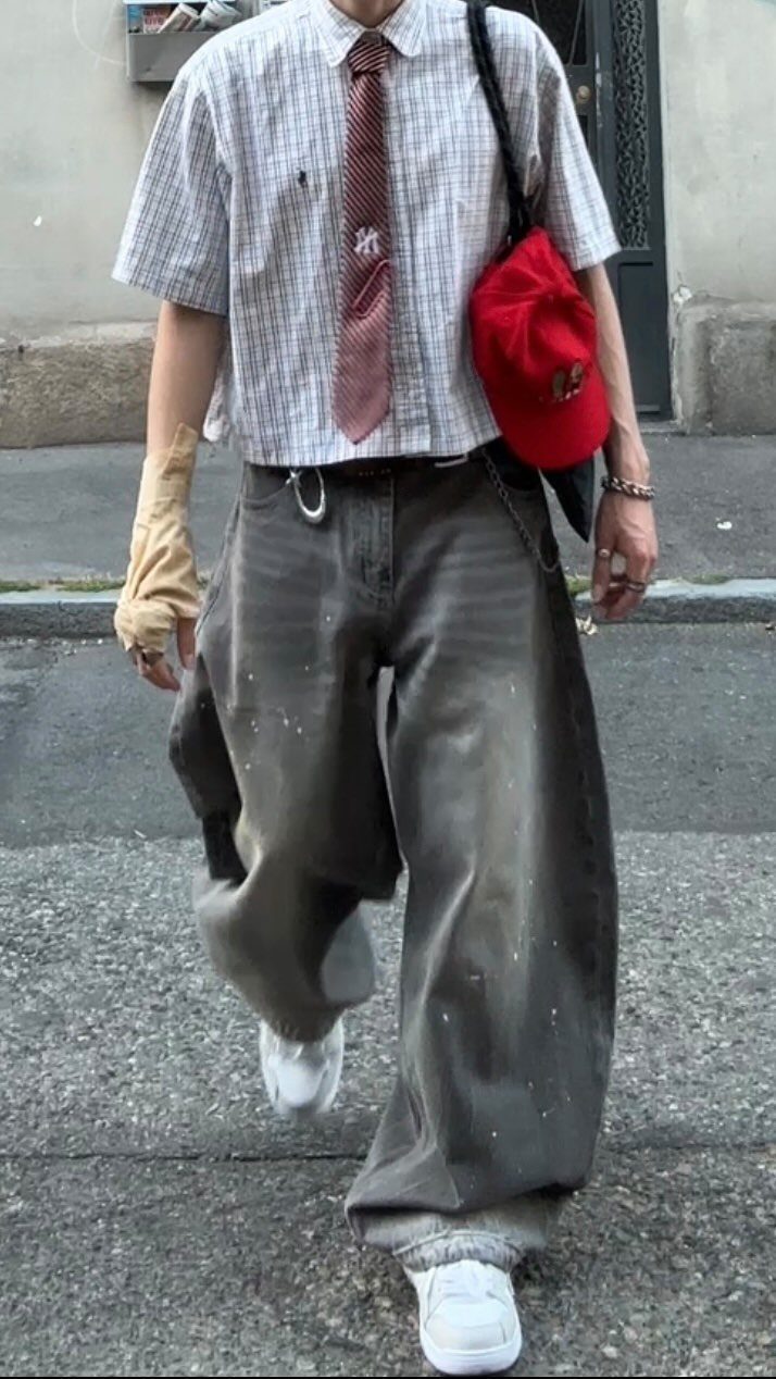 A person wearing baggy grey trousers, a checkered shirt, and a red necktie walking outdoors.