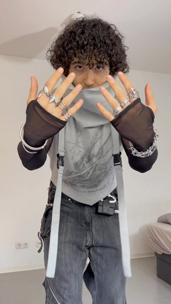 A person with curly hair wearing silver rings and grey baggy streetwear clothing.
