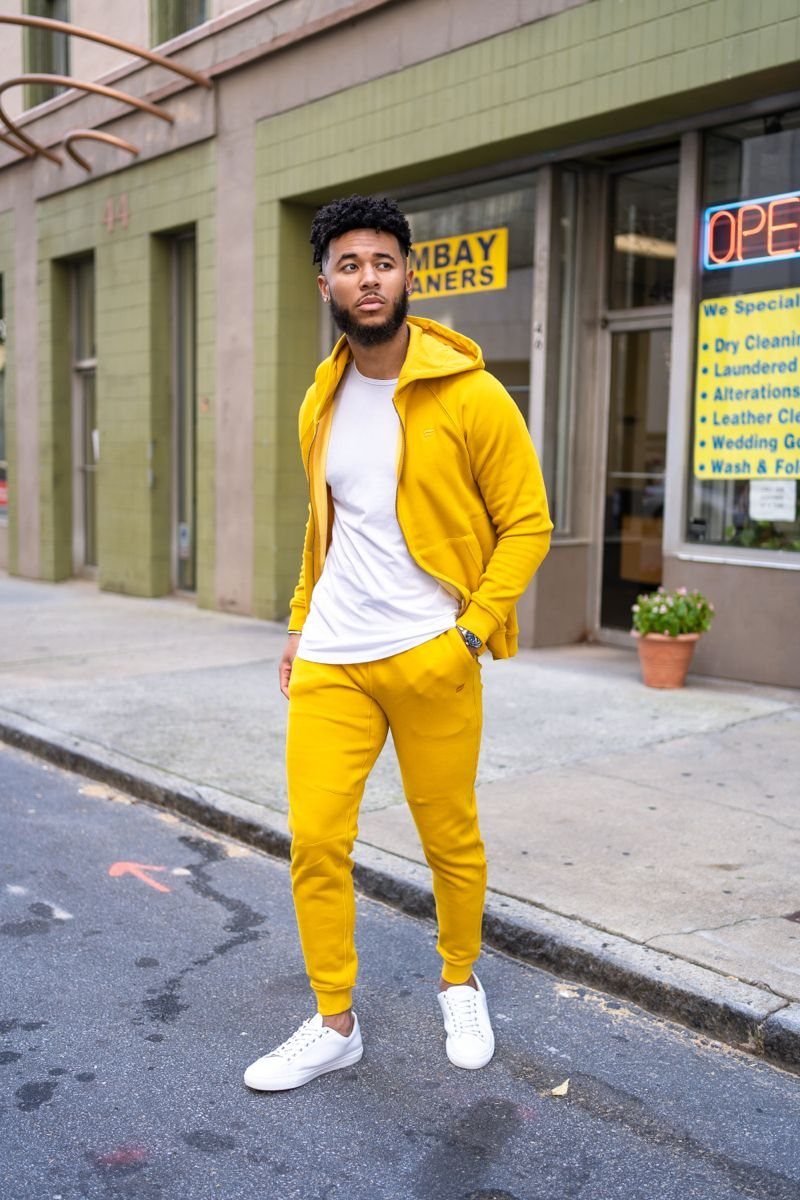 A man wearing a yellow zip-up hoodie and matching yellow joggers standing on a city street.