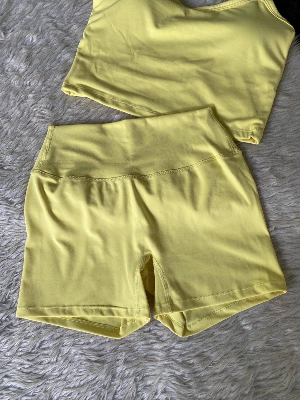 Yellow activewear tank top and matching high-waisted shorts laid on a white textured rug.